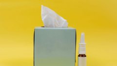A box of tissues and nasal spray to a yellow background