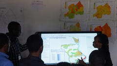 a group of people standing around a large computer screen that's displaying a map