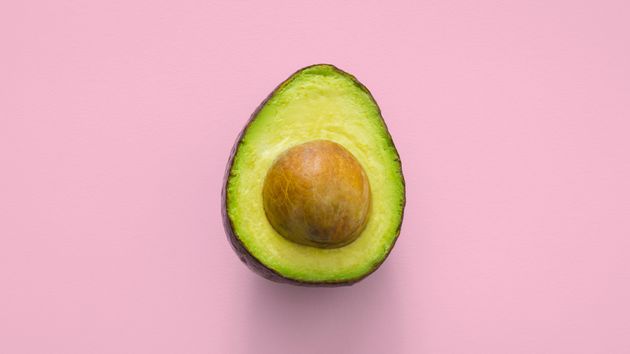 An avocado sliced in half on a pink background