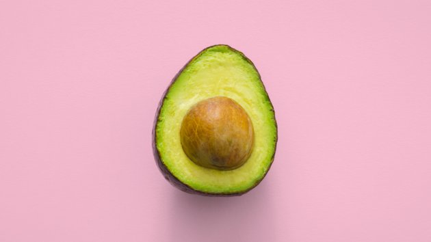 An avocado sliced in half on a pink background